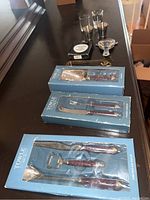 Three boxed Towle Silversmith bar tool sets arranged on a table alongside three shot glasses and a small silver-tone dish