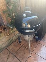 Front angled view of the black Weber kettle grill showing lid, handle, legs, and wheels.