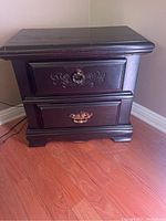 Front view of wooden nightstand showing two drawers with metal handles and carved details