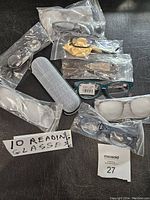 Ten new pairs of reading glasses in various styles and colors individually packaged, alongside a silver textured glasses case.