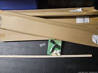 Four long cardboard boxes containing weed pullers with wooden handles and metal claw mechanisms.