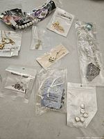Photo showing assorted jewelry items laid out including pearl bracelets, packaged earrings, charms, and pins