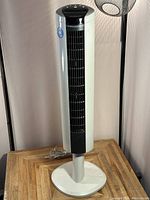 Tower fan and heater combo unit on a small wooden table, front and slightly right angle view showing control buttons and cord