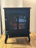 Front view of matte black electric fireplace stove with flame effect off, showing design with double door window and curved legs.