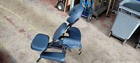 Side angle view of the portable massage chair showing the cushioned face cradle, arm rest, seat, and chest rest in royal blue on an aluminum frame.