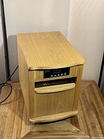 Front angled view showing wood casing, digital control panel, heating element grill, and caster wheels on bottom.