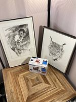 Overall lot including two framed black and white art prints and a boxed Philips digital photo frame on wood patterned floor surface against light wall