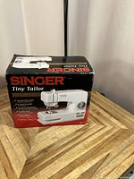 Photo shows the Singer Tiny Tailor sewing machine box from the front displaying product features and branding.