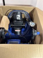 Top-down view of snow blower inside original box showing wheels, handle and chute