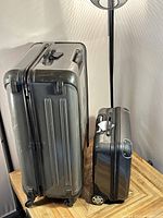 Two black hard-sided suitcases, one large and one small, positioned upright side by side showing wheels and handles.