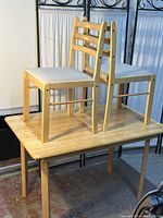 Photo showing the rectangular wooden table with two chairs placed on top, highlighting natural wood finish and chair seat upholstery.