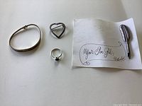Overall view of the four sterling silver jewelry pieces: bracelet, ring with red stone, heart brooch, and pen brooch with packaging.