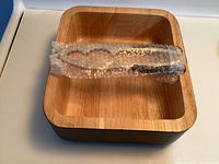 Nutcracker wrapped in bubble wrap inside a square wooden bowl with black outer surface and natural wood interior.