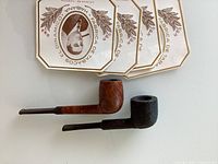 Two wooden cigar pipes placed next to four Cuban cigar labels with a portrait and text.