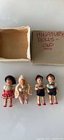 Four German miniature collectible dolls with their original box labeled 'MINIATURE DOLLS - OLD'. Dolls include two boys in traditional outfit, one girl in red dress, and one in pink outfit.