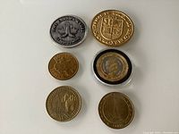 Six commemorative tokens arranged with various designs including Canada Games, cathedral, Eiffel Tower, Ireland, and Buffalo Days Regina Centennial