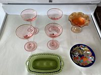 Full view of all items in the lot on white background, showing 4 pink martini glasses, green butter dish, Rosenthal plate, and carnival candy dish.