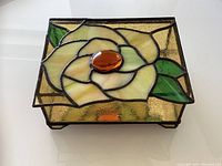 Top view showing the stained glass sunflower design with a central amber glass piece and surrounding yellow petals and green leaves on a textured background.