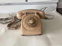 Beige MCM rotary dial telephone with handset and cables laid out on surface showing usage wear on the dial face.