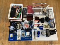 Overview of various office desk accessories arranged on wooden surface, including pens, pencils, rulers, notebooks, stamp, staplers, scissors, and more.