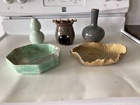 Five pottery pieces displayed on a kitchen counter: two vases, one brown oil warmer, and two decorative bowls.