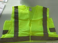 Three neon yellow safety vests with reflective strips laid flat on a surface showing front view.