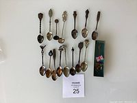 Group photo showing all 16 souvenir collectible spoons arranged in two rows on white background
