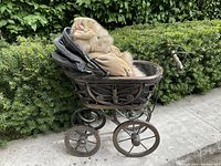 Side view of teddy bear sitting in antique metal baby carriage, showing textile and fur details on bear and metalwork on carriage