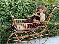 Wooden doll carriage with metal wheels, holding a large lifelike doll dressed in vintage clothing.