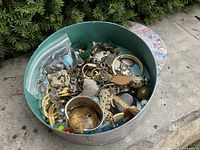 Top-down photo of round box filled with assorted costume jewelry pieces showing a variety of brooches, earrings, and bangles.