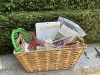Wide angled shot of entire woven basket filled with various knitting needles, knit loom, and packaged items