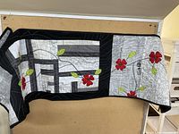Full view of folded black and white quilt runner with red flowers and green leaves, showing pattern and border.