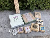 Photo showing the majority of the floral and themed stamps arranged on the ground including boxed sets and loose stamps. Multiple floral designs and other motifs such as a butterfly and snowman.