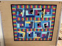 Full view of the quilt with geometric patchwork design and rainbow striped border pinned to a cork board.