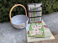 Full set of ceramic yarn bowl, crochet hooks in travel case, and two crochet books on concrete surface with bushes background.