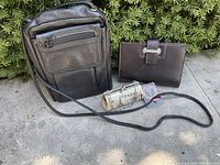 Photo showing Donofrio black leather crossbody bag, Paris-themed lipstick case, and brown Cutter & Buck notebook on outdoor surface
