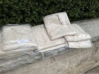 Four new cream-colored rayon/spandex dresses in plastic packaging, arranged on a stone ledge, showing size labels