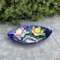 Full view of the oval cobalt blue ceramic dish with hand painted floral design showing pink, purple, yellow flowers and green leaves on brown branches.