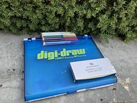 Blue Digi-Draw tracing board closed with Modern Design fountain pen box and colored pens on top, exterior view.