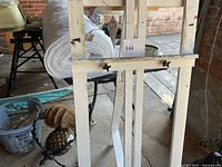Front and partial side view showing the painted white wooden easel with paint marks and stability features