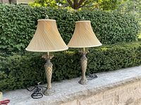 Pair of matching table lamps on stone ledge outdoors, showing full height and shape.