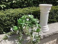 Overview showing white ceramic pedestal and bowl with faux flowers alongside outdoor greenery background.