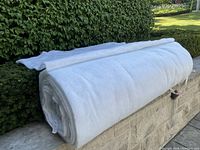 Large roll of white quilting batting laid on stone wall outdoors, showing size and thickness.