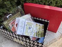 Photo of bankers box containing multiple packages and loose rubber stamps, some in plastic sleeves, some loose, showing variety of items.
