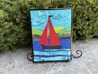 Full view of the framed quilted sailboat picture displayed on an easel outdoors.
