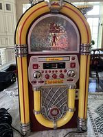 Front view of The Singing Machine karaoke player with jukebox styling, illuminated yellow and orange tubes, control panel and speaker grille.