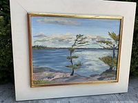 Frontal full view of the vintage oil painting framed, showing a water landscape with trees and cloudy sky.