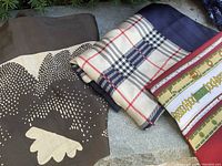 Three scarves laid out showing a brown and cream geometric scarf, beige plaid scarf with navy and red stripes, and a multi-color scarf with neon-inspired print.