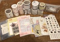 Photo showing multiple rolls of washi tape, sticker sheets, and decorative paper items arranged on a flat surface.