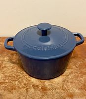Blue round cast iron casserole dish with lid on wooden surface, lid on